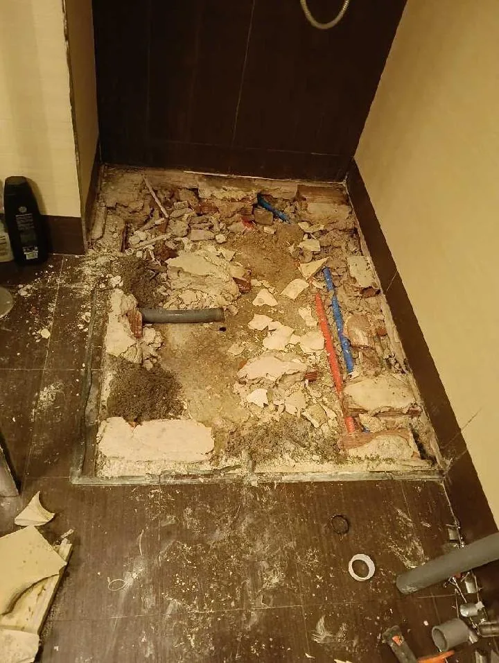 Suelo de ducha demolido con fontanería vista, antes de la reforma